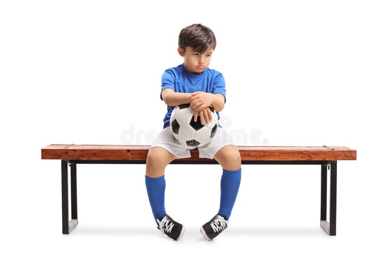 Petit footballer triste s'asseyant sur un banc en bois