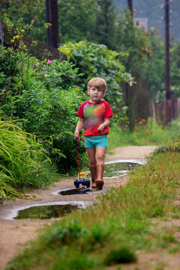 Petit Garçon Dans Des Bottes De Caoutchouc Tire Un Tracteur De Voitures De  Jouets De Jouet Sur Une Corde Photo stock - Image du regroupement, petit:  184264624