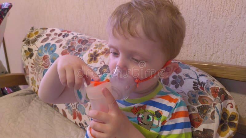 Petit garçon dans un masque, les traitements des voies respiratoires avec  un pulvérisateur à la maison. Siège bébé avec un nébulisateur dans sa  bouche, inhalateur, le traitement de la bronchite Photo Stock 