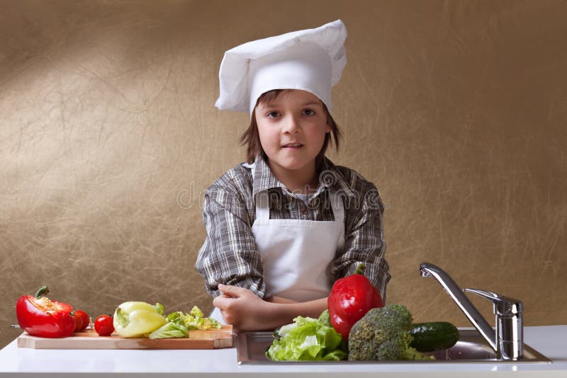 Petit garçon avec les légumes de lavage de chapeau de chef images stock Petit garçon avec les légumes de lavage de chapeau de chef images stock
