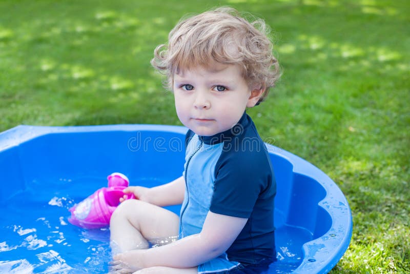 Petit garçon blond d'enfant en bas âge jouant avec de l'eau en été images stock Petit garçon blond d'enfant en bas âge jouant avec de l'eau en été images stock