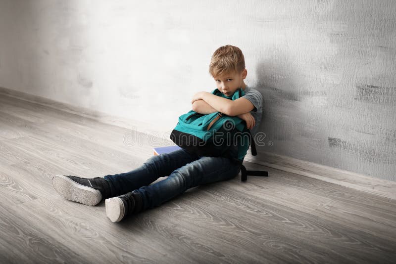 Petit garçon bouleversé avec le sac à dos se reposant sur le plancher à l'intérieur Intimidation à l'école image stock Petit garçon bouleversé avec le sac à dos se reposant sur le plancher à l'intérieur Intimidation à l'école image stock