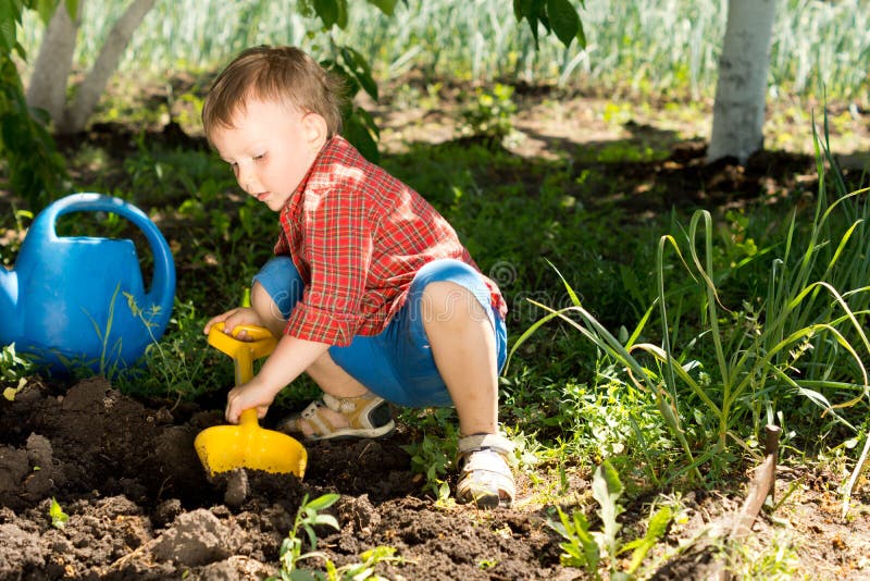 Little boy digging with a colourful yellow toy spade in fresh earth under the shade of a tree in the vegetable garden. Little boy digging with a colourful yellow toy spade in fresh earth under the shade of a tree in the vegetable garden