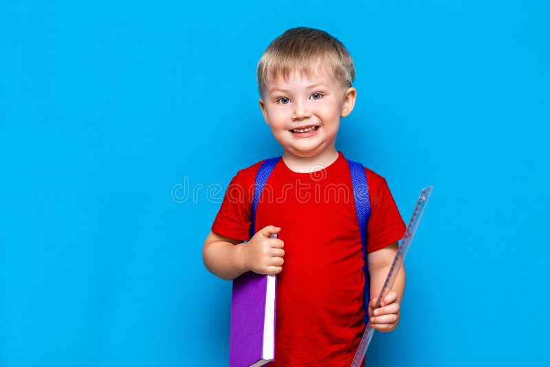 Petit garçon de sourire heureux avec les verres sur sa tête, livre dans des mains, cartable sur ses épaules De nouveau ? l'?cole photo libre de droits Petit garçon de sourire heureux avec les verres sur sa tête, livre dans des mains, cartable sur ses épaules De nouveau ? l'?cole photo libre de droits