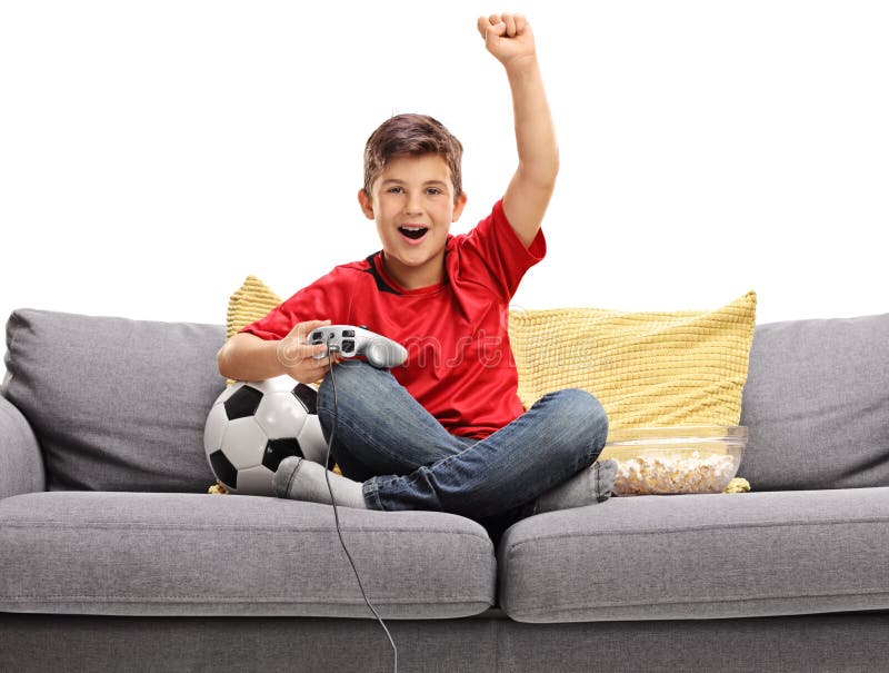 Petit garçon joyeux s'asseyant sur un sofa et jouant un jeu vidéo du football photographie stock Petit garçon joyeux s'asseyant sur un sofa et jouant un jeu vidéo du football photographie stock