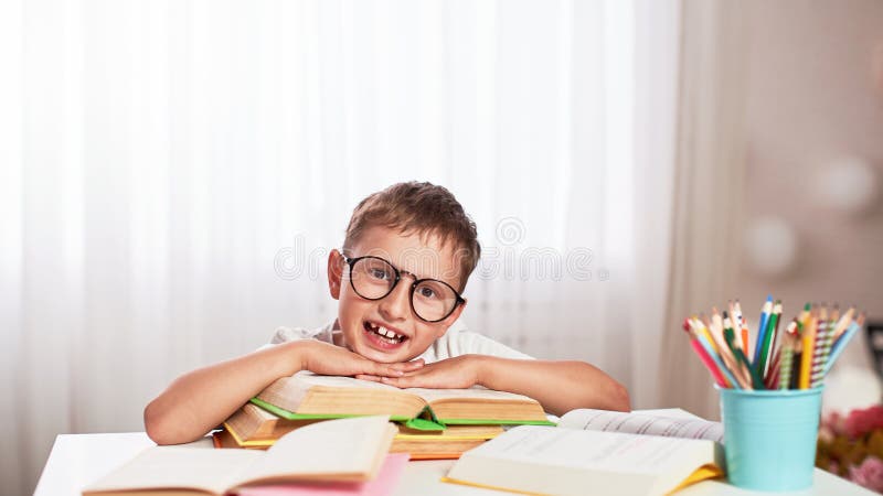 Petit garçon joyeux s'asseyant à la table avec des crayons et des manuels Élève heureux d'enfant faisant des devoirs à la table images stock