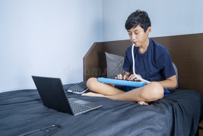 Petit garçon qui joue du pianica avec l'ordinateur portable sur le lit image stock
