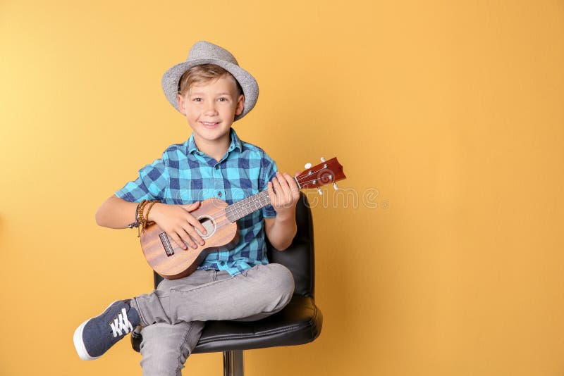 Petit garçon s'asseyant sur la chaise et jouant la guitare sur le fond de couleur photographie stock Petit garçon s'asseyant sur la chaise et jouant la guitare sur le fond de couleur photographie stock