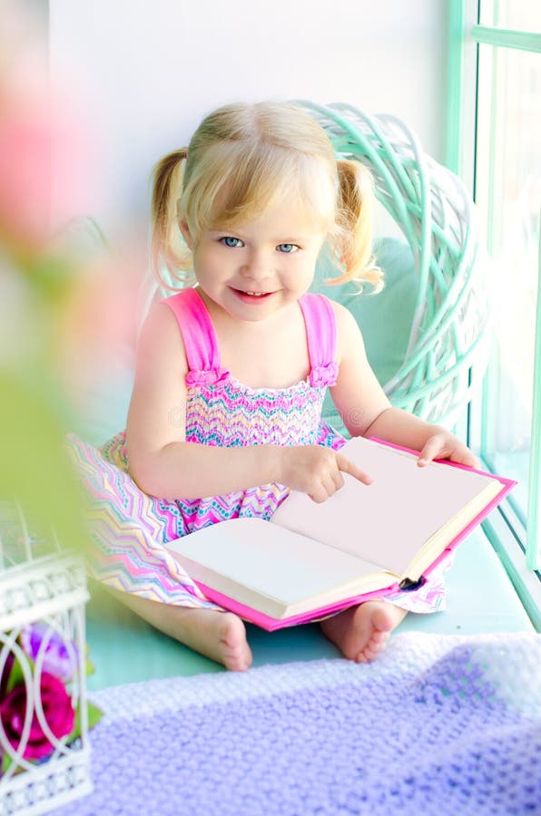 Petit livre de lecture drôle de fille près de fenêtre photographie stock libre de droits Petit livre de lecture drôle de fille près de fenêtre photographie stock libre de droits
