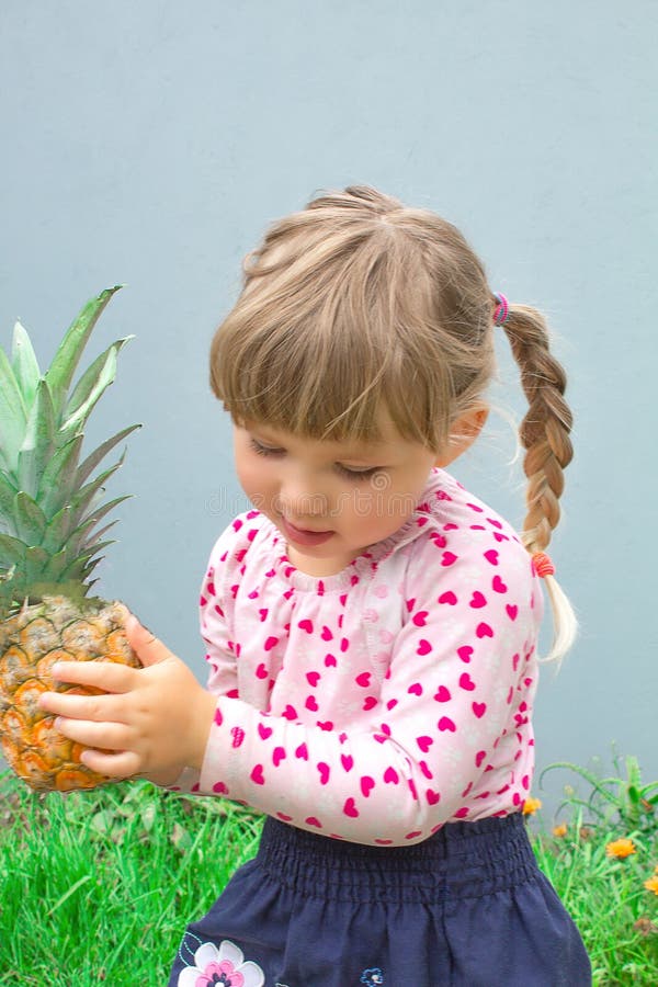 Petite belle fille tenant l'ananas en verres dans des ses mains Dans le jardin dehors photographie stock Petite belle fille tenant l'ananas en verres dans des ses mains Dans le jardin dehors photographie stock