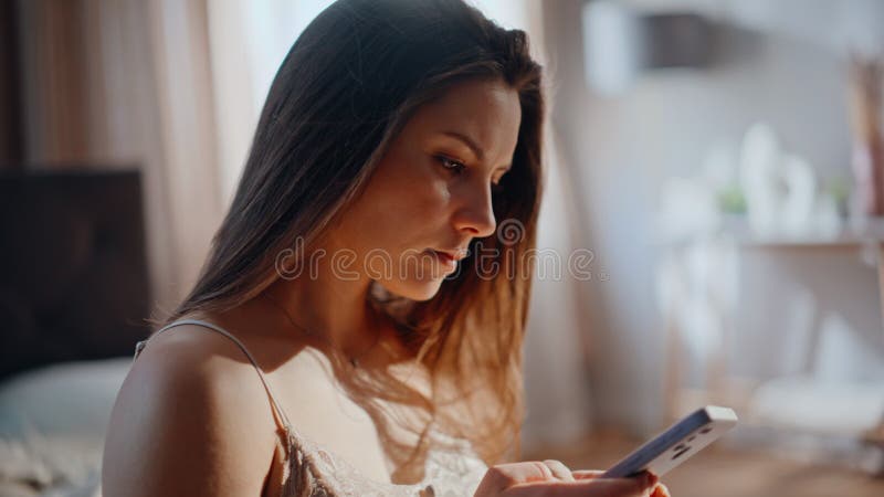 Petite dame textant téléphone cellulaire assis à la maison lit ensoleillé le matin closeup. Femme calme clips vidéos