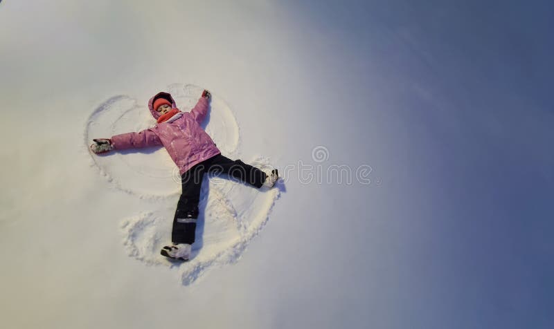 Petite fille allongée dans la neige et faisant l'angle vue dessus image stock