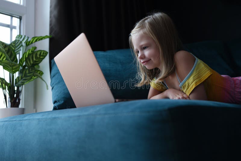 Petite fille allongée sur le canapé et regardant l'écran d'ordinateur portable. concept d'enseignement à domicile