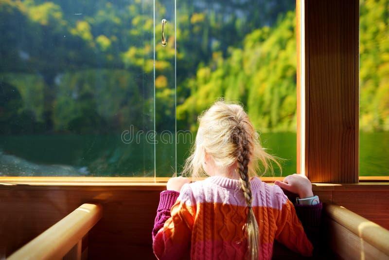 Petite fille appréciant une vue des eaux vert-foncé de Konigssee tout en voyageant en le bateau électrique image libre de droits Petite fille appréciant une vue des eaux vert-foncé de Konigssee tout en voyageant en le bateau électrique image libre de droits