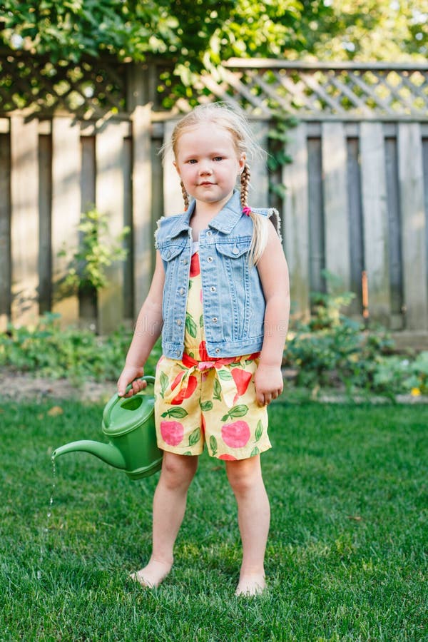 Petite fille arrosant les plantes vertes sur l'arrière-cour photos stock Petite fille arrosant les plantes vertes sur l'arrière-cour photos stock