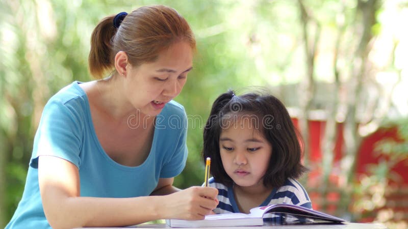 Petite fille asiatique avec la mère faisant le travail sur la table