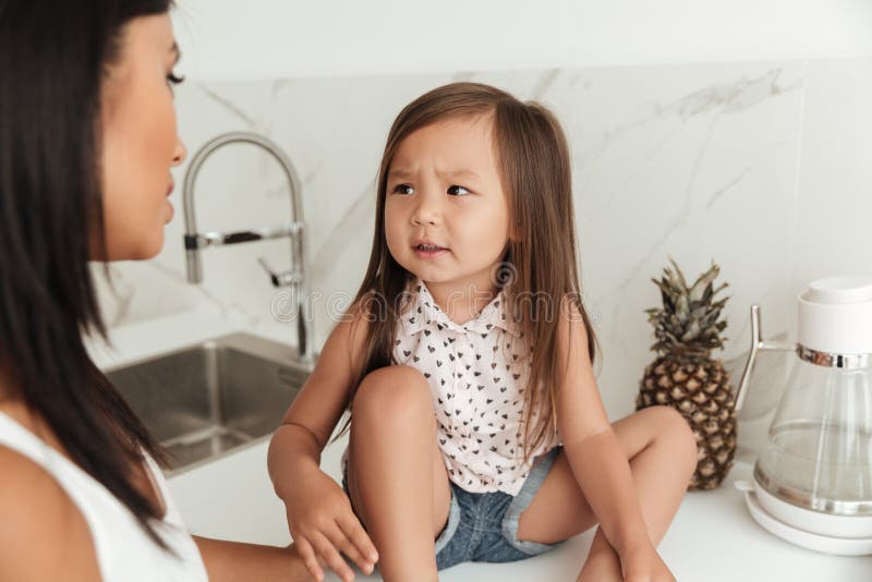 Petite fille asiatique avec le visage de froncement de sourcils regardant sa mère images stock Petite fille asiatique avec le visage de froncement de sourcils regardant sa mère images stock