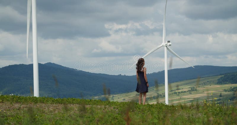Petite fille attrayante marchant près d'un champ avec des éoliennes alternatives d'énergie verte.