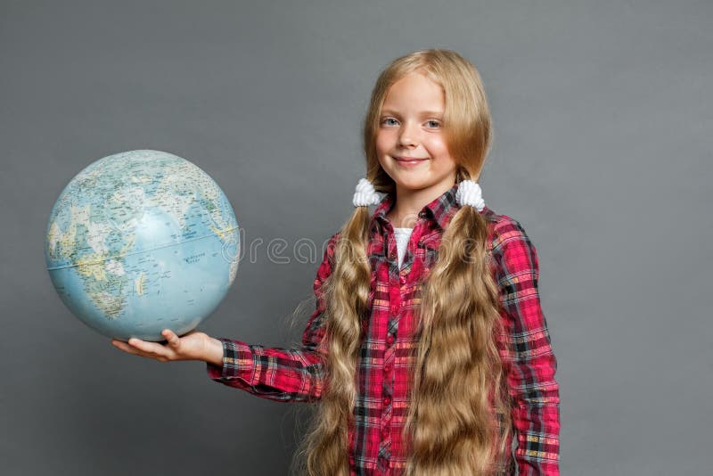 Petite fille avec des queues de cheval se tenant d'isolement sur le gris avec le globe regardant la caméra amicale image stock Petite fille avec des queues de cheval se tenant d'isolement sur le gris avec le globe regardant la caméra amicale image stock