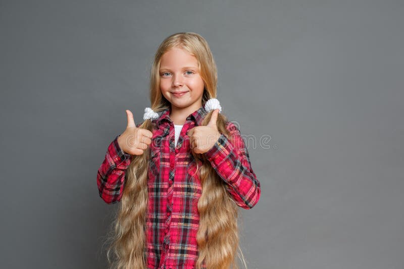 Petite fille avec des queues de cheval se tenant d'isolement sur les pouces de représentation gris vers le haut de regarder la ca images stock Petite fille avec des queues de cheval se tenant d'isolement sur les pouces de représentation gris vers le haut de regarder la ca images stock