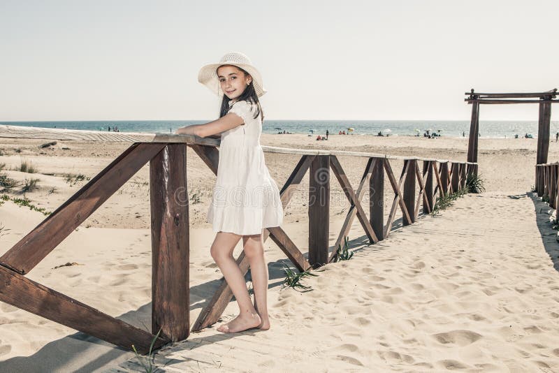 Petite fille avec le chapeau se penchant contre la balustrade en bois sur la plage photo stock Petite fille avec le chapeau se penchant contre la balustrade en bois sur la plage photo stock