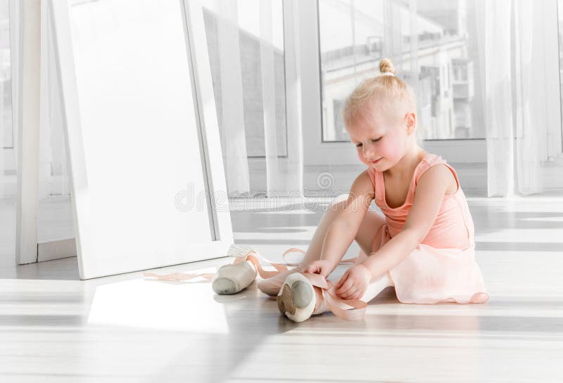Petite fille blonde mignonne s'asseyant sur le plancher et attachant des chaussures de ballet photos libres de droits Petite fille blonde mignonne s'asseyant sur le plancher et attachant des chaussures de ballet photos libres de droits