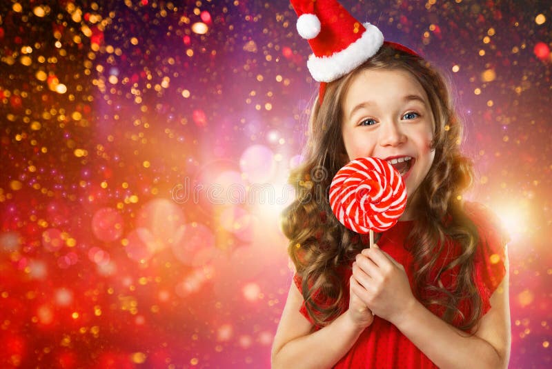 Petite fille dans le chapeau du ` s de Santa avec la sucrerie sur le fond de lumières images stock Petite fille dans le chapeau du ` s de Santa avec la sucrerie sur le fond de lumières images stock