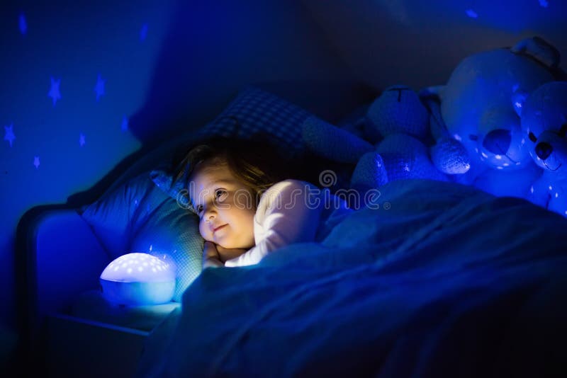 Petite fille dans le lit avec la lampe de nuit photos libres de droits Petite fille dans le lit avec la lampe de nuit photos libres de droits