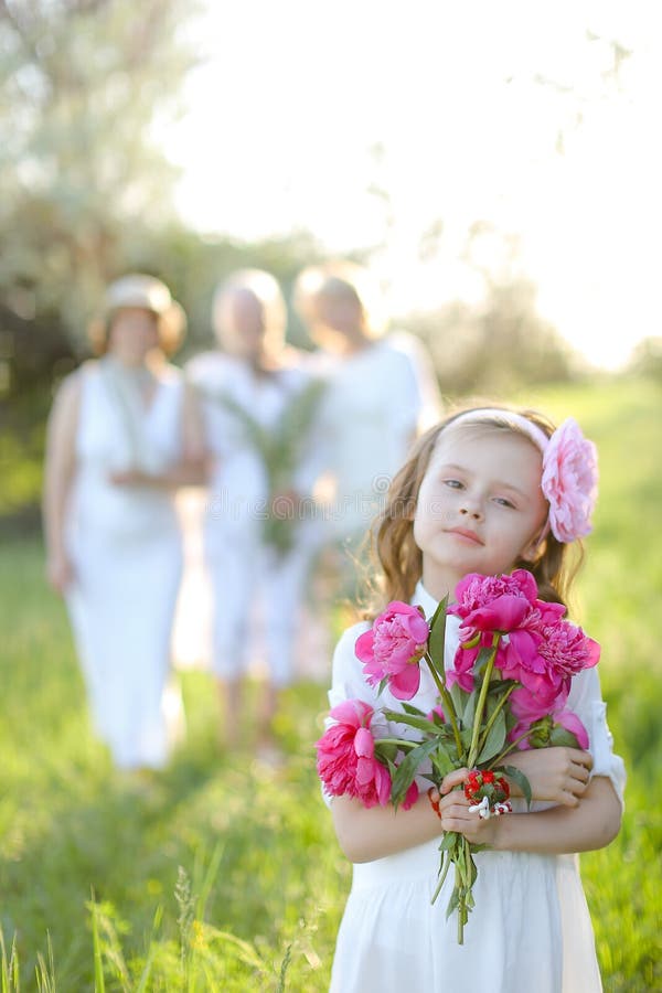 Petite fille en robe blanche gardant des fleurs floues famille en arrière-plan. photo libre de droits