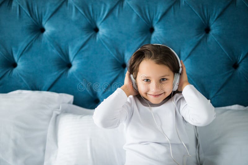 Petite fille heureuse dans des pyjamas écoutant la musique tout en se reposant dans son lit photo libre de droits Petite fille heureuse dans des pyjamas écoutant la musique tout en se reposant dans son lit photo libre de droits