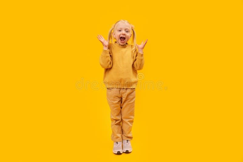 Petite fille hurle ou s'étonne. portrait complet de la petite fille de l'école maternelle en costume jaune sur fond jaune image stock