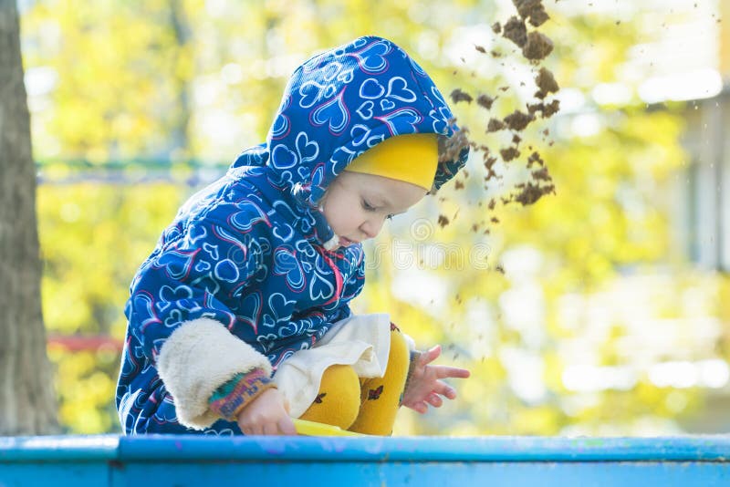 Petite fille jouant dans le bac à sable dehors au bosquet de jaune d'automne et au fond de feuilles d'arbres image stock