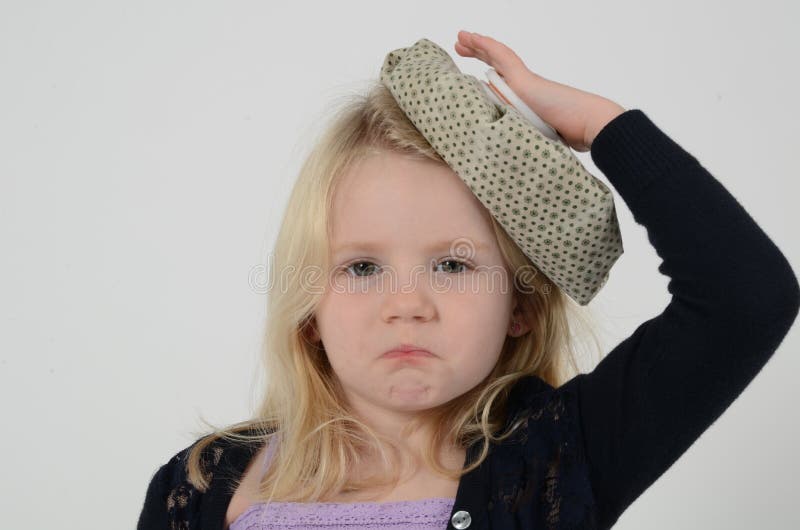 Sick little blonde girl with pouting lips holds ice bag on head and looks sad. Sick little blonde girl with pouting lips holds ice bag on head and looks sad