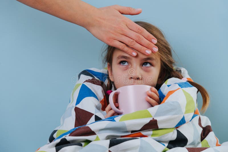 Petite fille malade avec un rhume commun assise sous une couverture avec du thé chaud