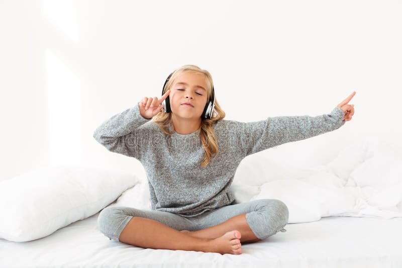 Petite fille mignonne dans des pyjamas gris écoutant la musique avec fermé images stock Petite fille mignonne dans des pyjamas gris écoutant la musique avec fermé images stock
