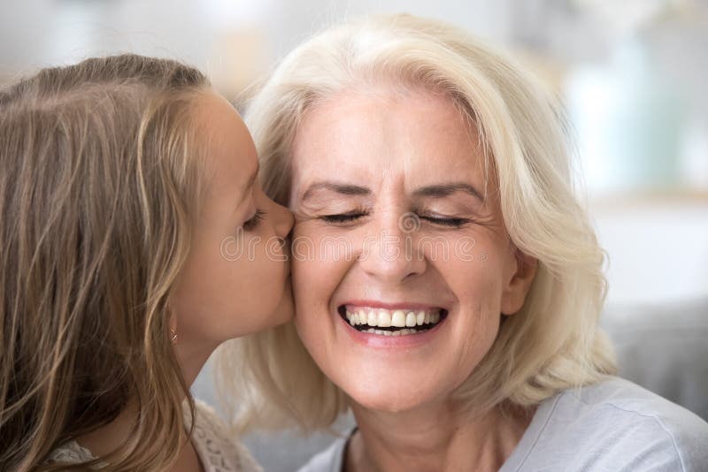 Petite petite-fille mignonne embrassant la vieille grand-mère de sourire sur le che photo stock Petite petite-fille mignonne embrassant la vieille grand-mère de sourire sur le che photo stock