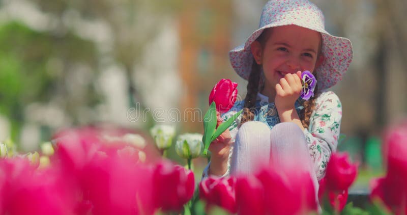 Petite fille mignonne souriant et appréciant fleurir jardin de tulipes et violettes banque de vidéos