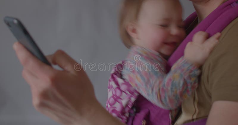 Petite fille mignonne sourit avec enthousiasme tout en étant assise dans un porte-bébé ergonomique.