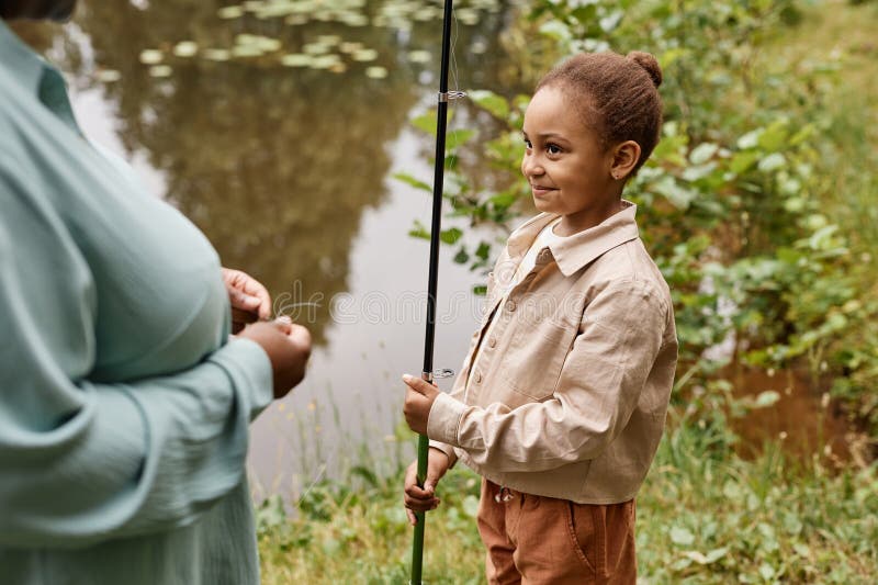 Petite fille noire tenant une canne de pêche et souriant joyeusement photos stock