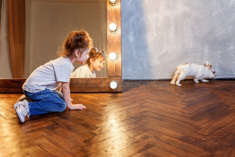 Petite fille s'asseyant sur le plancher et jouant avec le lapin blanc de lapin dans la chambre moderne au-dessus du miroir photos libres de droits Petite fille s'asseyant sur le plancher et jouant avec le lapin blanc de lapin dans la chambre moderne au-dessus du miroir photos libres de droits