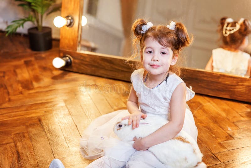 Petite fille s'asseyant sur le plancher et jouant avec le lapin blanc de lapin dans la chambre moderne au-dessus du miroir images stock Petite fille s'asseyant sur le plancher et jouant avec le lapin blanc de lapin dans la chambre moderne au-dessus du miroir images stock
