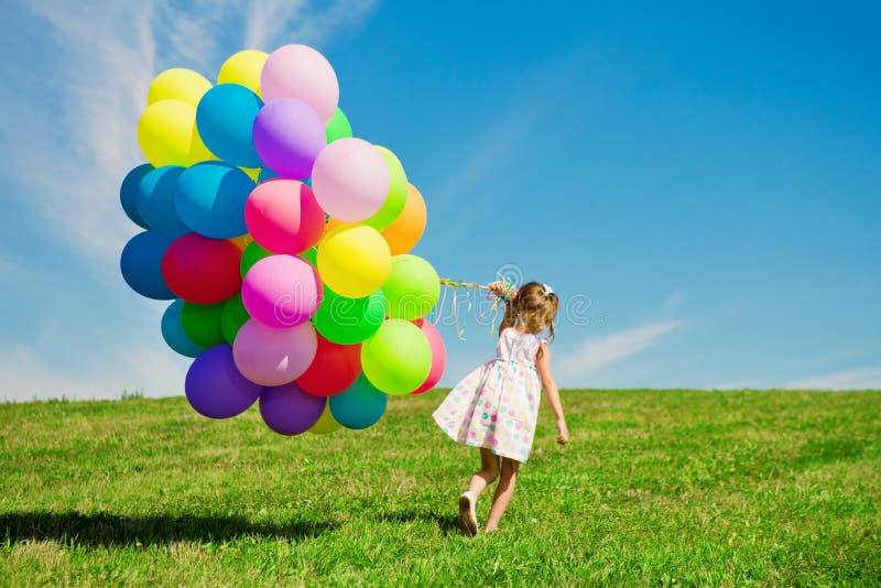 Petite fille tenant les ballons colorés. Enfant jouant sur un vert