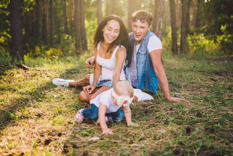 Petite fille un an sur le fond des parents se reposant se trouvant sur l'herbe apprenant ? marcher sur la nature en parc Les prem photo libre de droits Petite fille un an sur le fond des parents se reposant se trouvant sur l'herbe apprenant ? marcher sur la nature en parc Les prem photo libre de droits