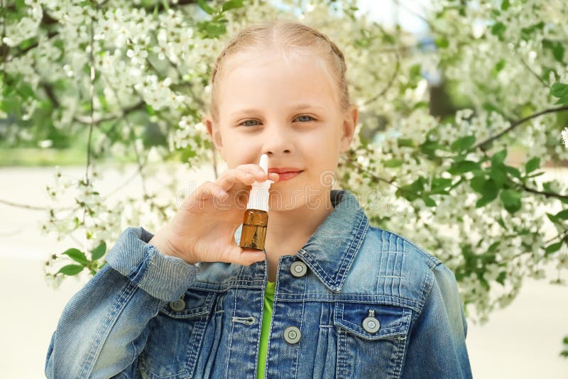 Petite fille utilisant des gouttes pour le nez près d'arbre de floraison Concept d'allergie