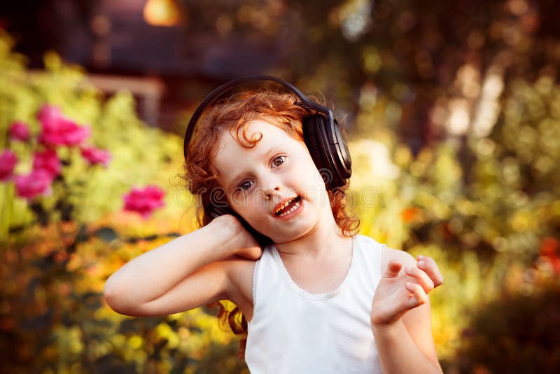 Petite fille écoutant la musique sur des écouteurs en parc d'été images libres de droits Petite fille écoutant la musique sur des écouteurs en parc d'été images libres de droits