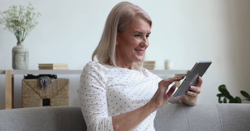 Petite-mère d'âge moyen heureuse utilisant une tablette numérique assise sur un canapé. clips vidéos