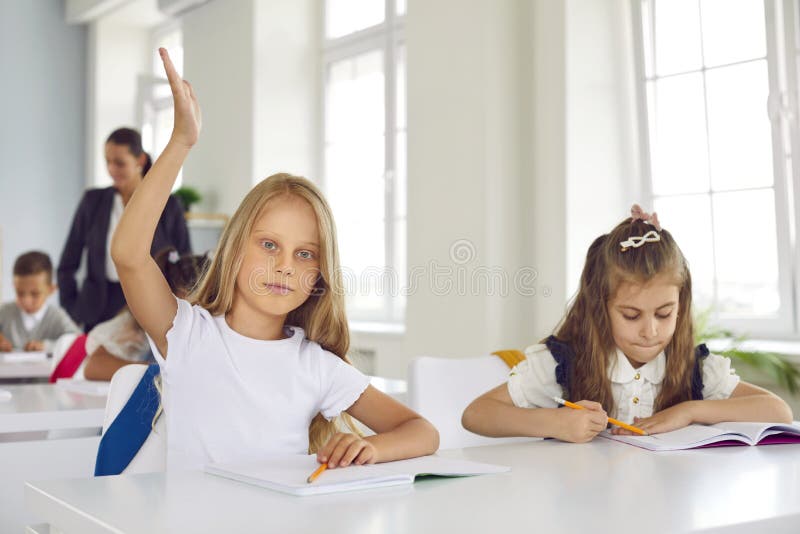 Petite écolière intelligente lève la main pendant la leçon voulant répondre à la question des enseignants.