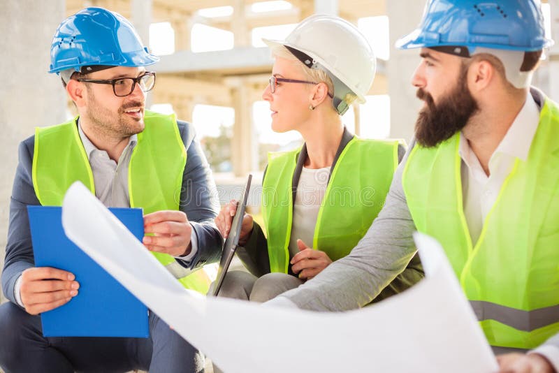 Petite ?quipe d'architectes visitant un chantier de construction, regardant des mod?les photographie stock Petite ?quipe d'architectes visitant un chantier de construction, regardant des mod?les photographie stock