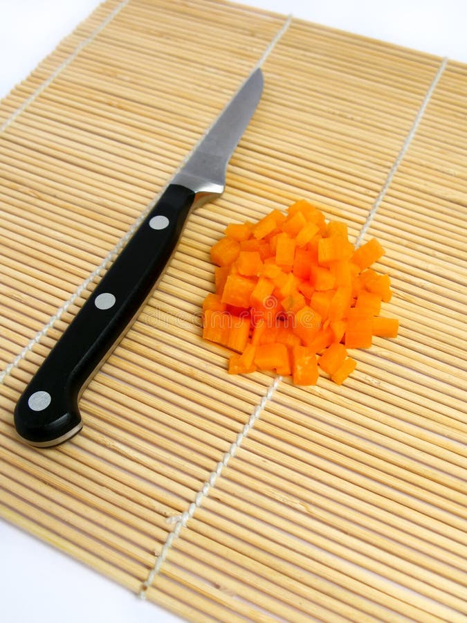 Carrot cut in small cubes , knife behind the carrot, and a bamboo carpet background. Carrot cut in small cubes , knife behind the carrot, and a bamboo carpet background.