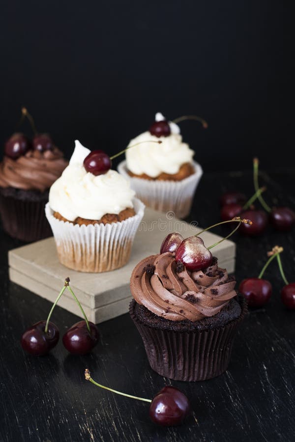 Petits gâteaux délicieux de chocolat et de vanille avec des cerises sur un blac images stock Petits gâteaux délicieux de chocolat et de vanille avec des cerises sur un blac images stock